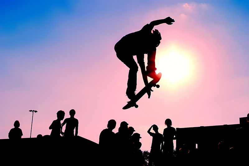 Jumping skateboarder silhouette over scenic sunset sky backgroun